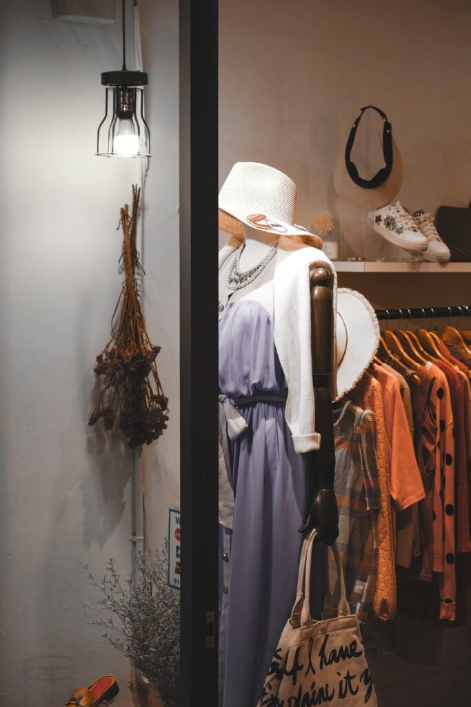 Mannequin in a boutique in Larnaca, Cyprus, wearing a lavender dress and wide-brimmed hat, with assorted clothing in the background and dried botanicals on the side.