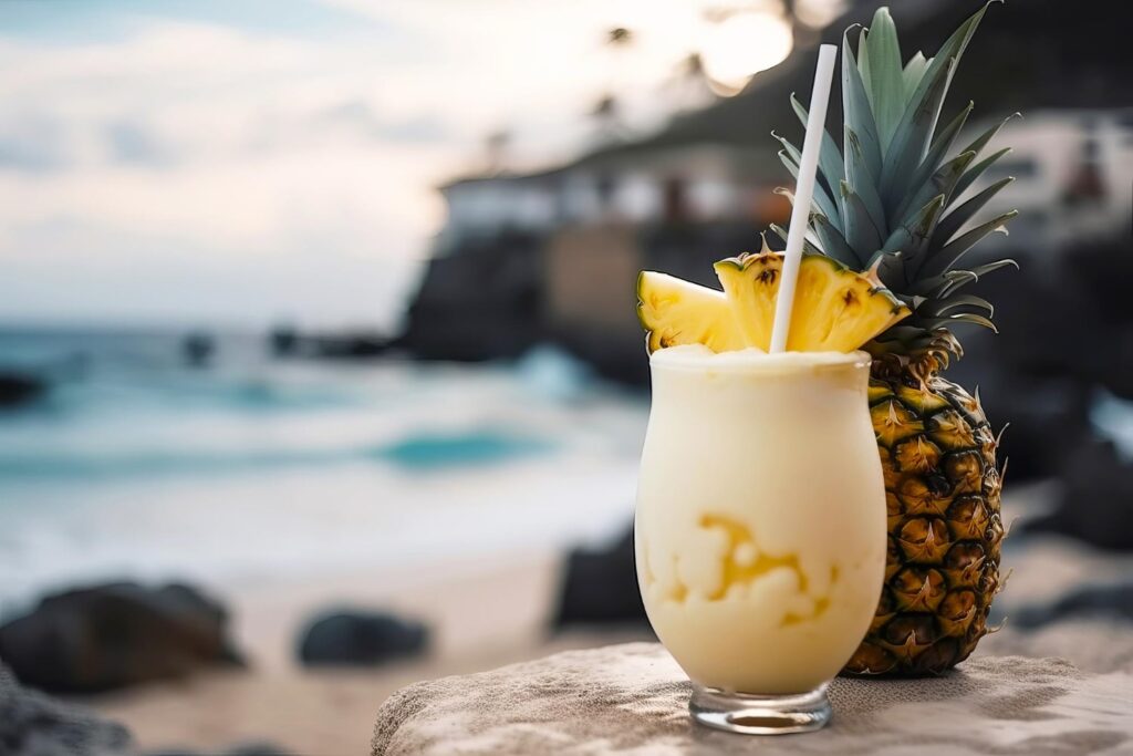 Frothy Piña Colada with pineapple garnish on a beach with waves in the background.